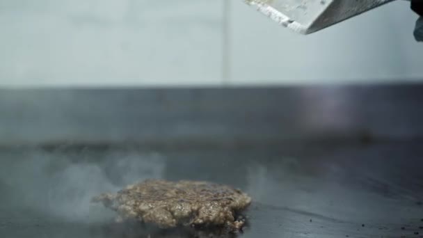 Casual bar, μάγειρας με γάντια αναποδογυρίζει με σπάτουλα για το μαγείρεμα ζουμερό χοιρινό μετάλλιο για burger σε σχάρες φόντο καπνού στην κουζίνα του cafe — Αρχείο Βίντεο