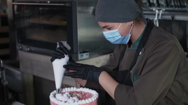 戴着医疗面罩和手套的可爱女式糕点厨师在餐厅厨房里准备美味的甜点，用糕点袋装饰，新鲜烘焙的奶油蛋糕 — 图库视频影像