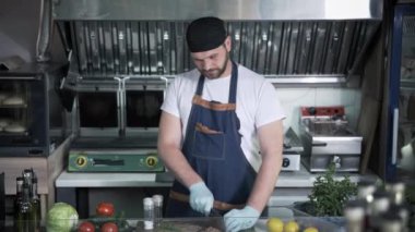 Kafe ya da restoranın mutfağında tıbbi maske takan erkek şef karantina sırasında hamburger için et hazırlıyor.