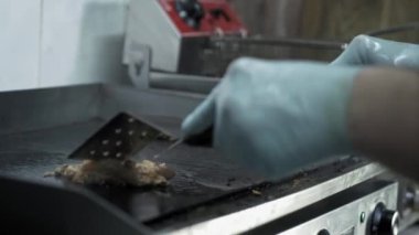 Izgarada et pişirmek, eldiven giymiş erkek aşçı elleri, fast food mutfağında dumanın arka planını kızartırken sulu et dilimlerini çevirir.