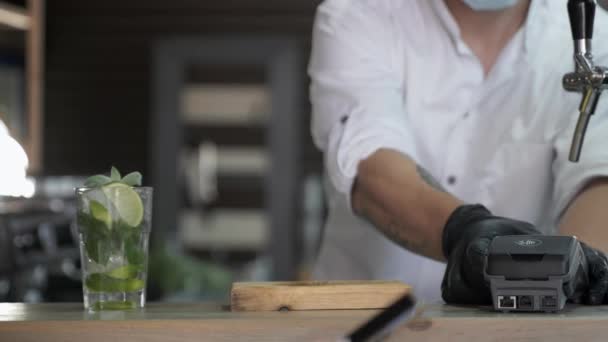 Vorsichtshalber bezahlt eine glückliche Käuferin in medizinischer Maske ihren Cocktail per Smartphone per kontaktlosem Bezahlen an der Bar — Stockvideo