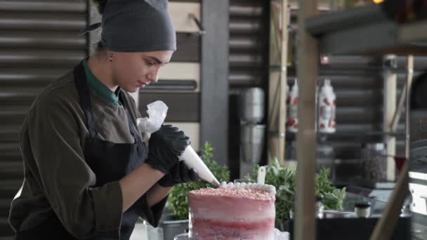 Confitería, linda chica panadero adulto encantadora decora delicioso pastel hecho a mano con crema usando bolsa de pastelería en la pastelería comercial — Vídeos de Stock