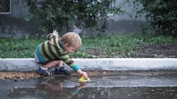 Entretenimientos para los niños, pequeño niño simpotic masculino se divierte jugando en la piscina con ktka de goma para nadar en el patio después de la lluvia — Vídeos de Stock