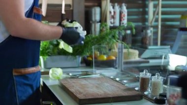 Mutfak, eldivenli erkek aşçı restoran veya kafe mutfağında salata hazırlamak için kesim tahtasına sebze koyar.