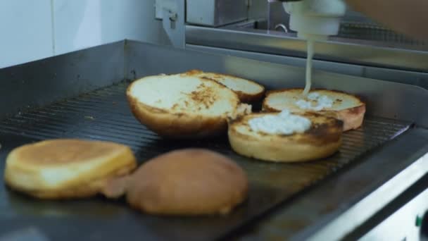 Koken hamburger, koken in handschoenen giet saus uit een fles in broodjes voor het maken van gegrilde hamburger in keuken cafe — Stockvideo