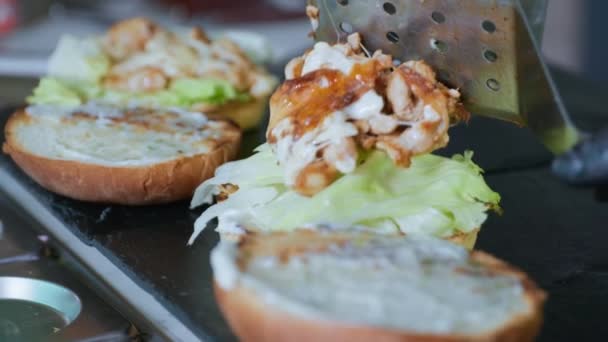 Junk food, fresh fragrant buns with sauce and lettuce are laid out using spatula to prepare food, fried minced meat with cheese for making burger or cheeseburger in kitchen — Stock Video