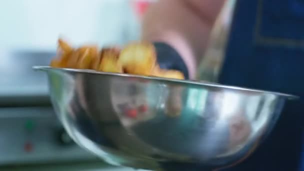 Man kock kokta i handskar rör aptitretande stekt potatis i olja i skål med kryddor i restaurang eller café kök — Stockvideo