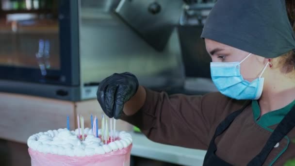 Retrato de hermosa cocinera en máscara médica y guantes prepara pastel de cumpleaños para la fiesta de cumpleaños en la cafetería — Vídeo de stock