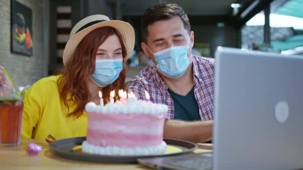 Distanza sociale, gioioso uomo e donna in maschere mediche per proteggersi da virus e infezioni durante la pandemia divertirsi a chattare con gli amici tramite video chat sul computer portatile — Video Stock