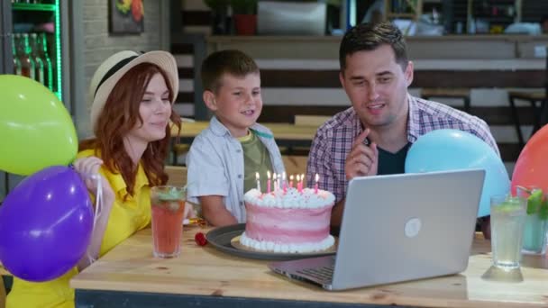 Charming family have fun celebrating online birthday of their beloved son, chatting through video calls with friends blowing out candles on a birthday cake — Stock Video