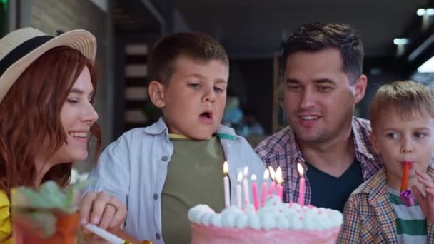 Вечірка на день народження, милі чоловічі діти зі своїми люблячими батьками і братом з повітряними кулями і трубами святкують його день народження вибухають свічки на смачному торті і кусає святковий десерт — стокове відео