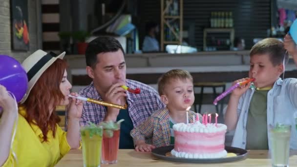 Festa feliz, bonito menino com seus pais amorosos e irmão com balões e tubos comemora seu aniversário apaga velas no delicioso bolo e morde sobremesa festiva — Vídeo de Stock