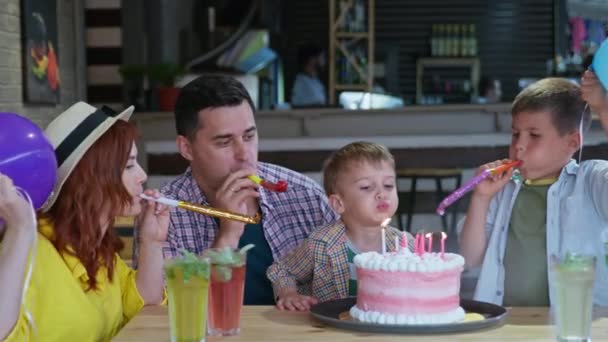 Feliz fiesta, lindo niño varón con sus padres cariñosos y hermano con globos y tuberías celebra su cumpleaños sopla velas en delicioso pastel y muerde postre festivo — Vídeo de stock