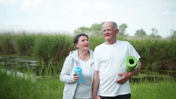 Fröhliche alte Mann und Frau kümmern sich um ihre Gesundheit gehen Händchenhalten nach einem morgendlichen Training im Freien — Stockvideo