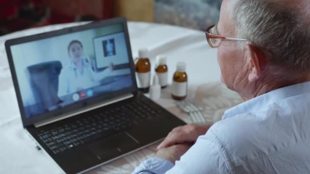 Онлайн консультация, пожилой мужчина пенсионера с плохим здоровьем беседует с врачом через видео связи с использованием современных технологий — стоковое видео