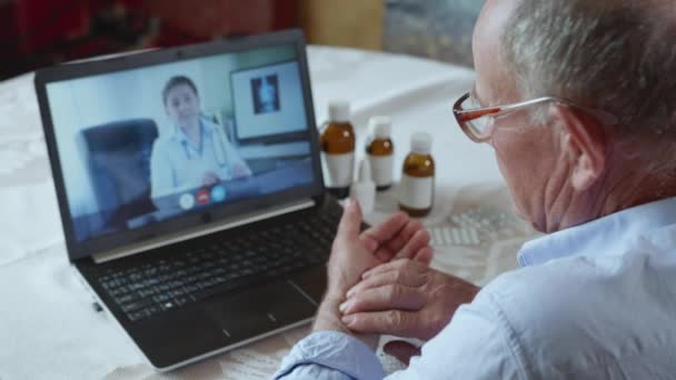 Saúde ruim, idoso aposentado paciente masculino com óculos para visão consulta médico on-line em videochamada usando tecnologia moderna, homem idoso mede seu pulso — Vídeo de Stock