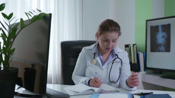 Il dottore in linea, il dipendente di ospedale professionale femminile comunica con paziente su smartphone consulta su computer in ufficio medico per semplicità di freddo — Video Stock