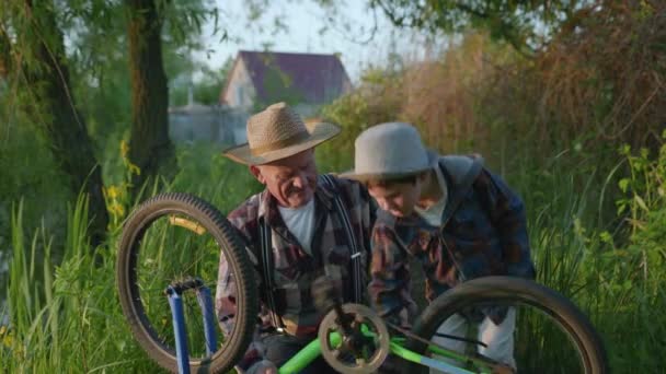 Levensstijl, gelukkige oudere man en charmante ginny kleinzoon in hoeden peddel tijd doorbrengen spinnen wielen en pedalen van fiets buiten tijdens familie outdoor recreatie — Stockvideo