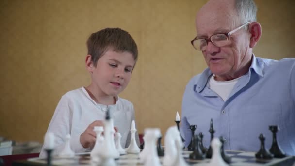 Vzdělávací hry, roztomilé veselé mužské dítě baví se se svým starším dědečkem v brýlích pro zrak v šachu — Stock video