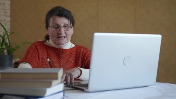 Modern elderly woman writes information in a notebook while studying online using modern technology — Stock Video