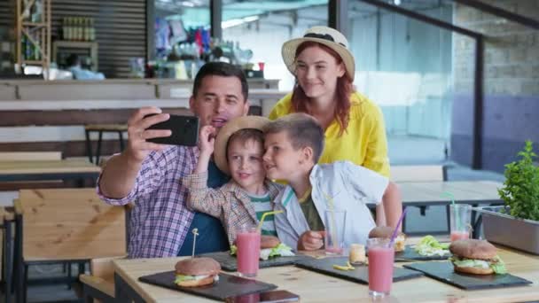 Atraktivní rodiče, muž a žena, spolu se svými mužskými dětmi, vychutnat rodinnou večeři v restauraci fast food a mají videohovory — Stock video