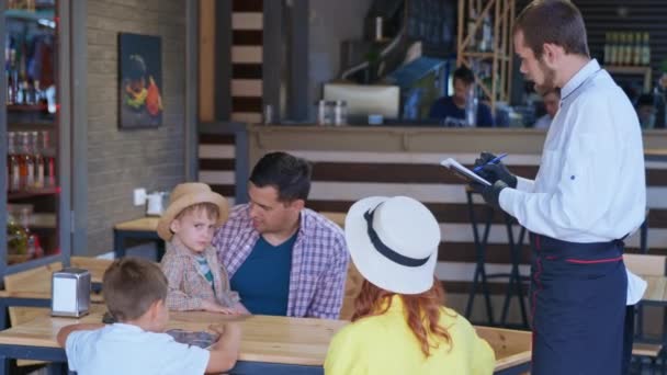 Семейный отдых, счастливые родители с маленькими детьми мужского пола наслаждаются совместным отдыхом в кафе — стоковое видео