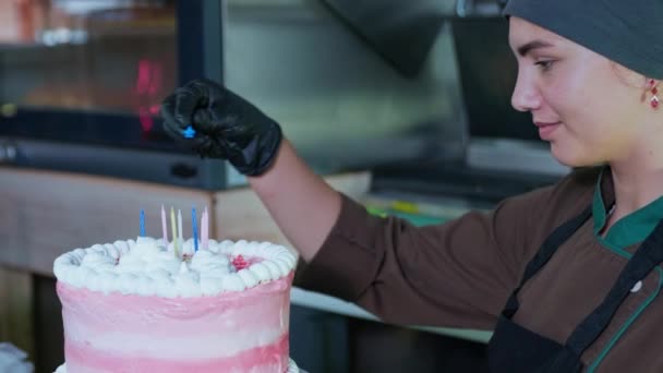 Hermosa pastelera femenina decora pastel festivo con velas para felicitar a los visitantes en la cafetería, panadería — Vídeos de Stock