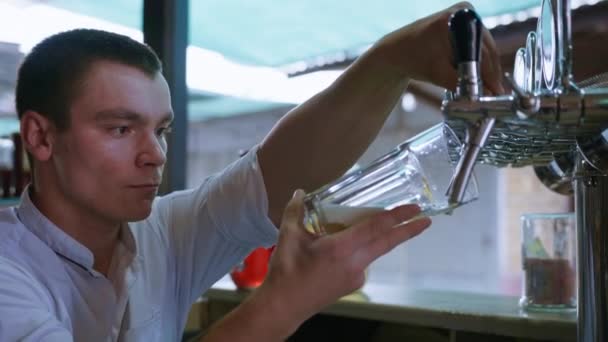 Bebida fresca, garçom masculino derrama cerveja fresca e espumosa em vidro de barril usando cerveja em um pub popular — Vídeo de Stock