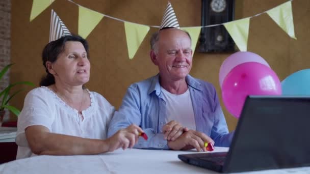 Virtuele communicatie, vrolijk bejaardenpaar met caps, ballonnen en kleine handjes in hun handen hebben plezier in het creëren van een feestelijke sfeer praten met hun kinderen of kleinkinderen met behulp van een video — Stockvideo