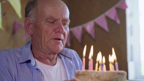 Old handsome man of retirement age has fun at birthday party and enjoys blowing out candles on festive sweet cake — Stock Video