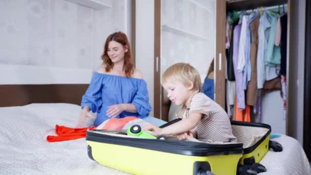 Voyage des enfants, charmant petit garçon mignon s'amuse avec sa mère attentionnée aidant parent femelle recueillir des vêtements et des jouets pour le voyage en famille pendant les vacances d'été le week-end — Video