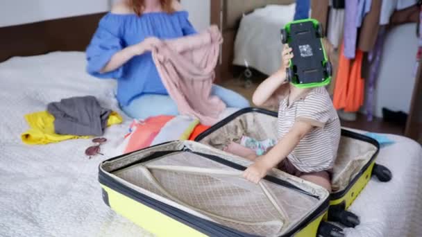 Pilny mężczyzna dziecko pomaga jego ukochanej matce zbierać rzeczy i zabawki w torbie podróżnej, mały chłopiec zbiera swój ukochany plastikowy samochód w walizce na rodzinny wyjazd do letniskowego kurortu podczas wakacji — Wideo stockowe