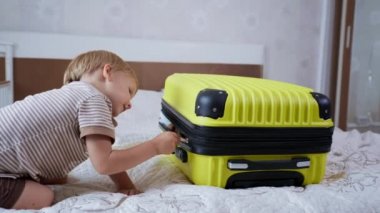 Çocuklar seyahat ediyor, neşeli küçük çocuk tatilde valizlerle oynuyor. Tatil gezisi için ailesiyle bir sürü şey alıyor.