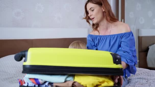 有爱心的妈妈和她的男孩儿会很开心地把旅行袋放在沙发上的房间里，供家人度假 — 图库视频影像