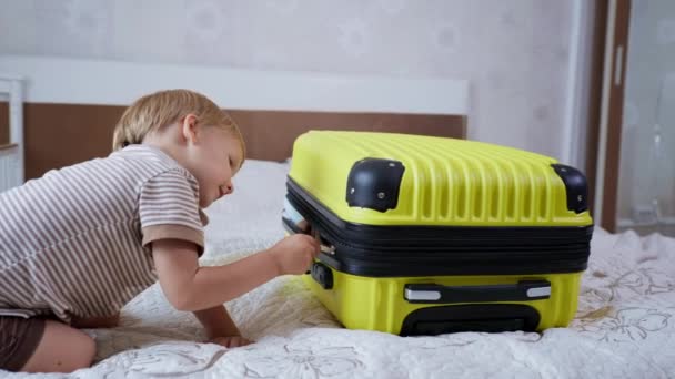 Les enfants voyagent, joyeux petit enfant avoir du plaisir à jouer avec les bagages pour les vacances plein de choses pour le voyage de vacances avec ses parents — Video