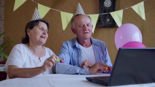 home isolation, joyful grandparents with balloons and horns have fun celebrating a birthday online chatting with friends and family via video calling on a laptop