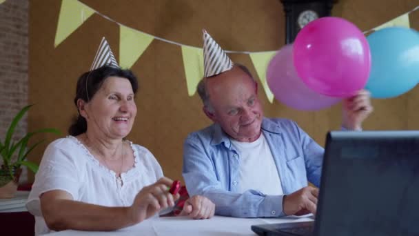 Communicatie op afstand, bejaarde grootouders met vakantiepetten en pijpen communiceren online met vrienden of familie op verjaardagsfeestje met behulp van webcamera op laptop tijdens sociale afstand en zelfisolatie — Stockvideo