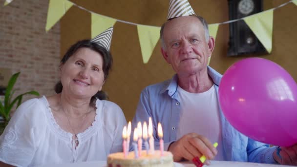 İzolasyon partisi, emeklilik yaşında yaşlı kadın ve adam şapkalı ve mumlu doğum günü pastalı modern video iletişim teknolojisini laptopta kullanın ve doğum gününü tek başına kutlayın. — Stok video