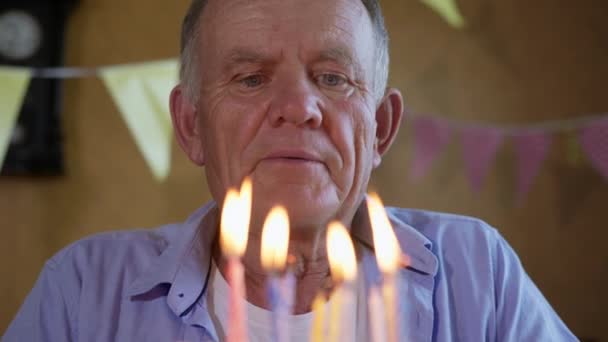 Atraktivní přátelský starší muž si užívá své narozeniny a šťastně sfoukne slavnostní svíčky na dort — Stock video