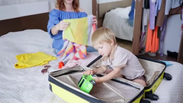 Niños viajan, alegre querido niño pequeño macho se divierte con su padre femenino cuidado recoger ropa y juguetes para el viaje familiar en las vacaciones de verano en fin de semana aplaudir sus manos y dar cinco a cada uno — Vídeos de Stock