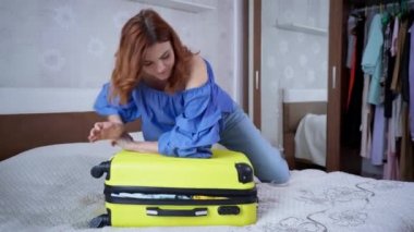 Genç ve güzel bir kız seyahate hazırlanıyor ve dolup taşan bir bavulu yaz tatili için kıyafetlerle kapatmaya çalışıyor.