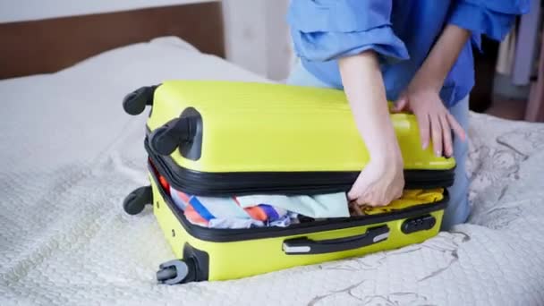 Luggage for vacation, young woman is going to travel and trying to close her suitcase with things and clothes, sits on top and zips up on her travel bag — Stock Video