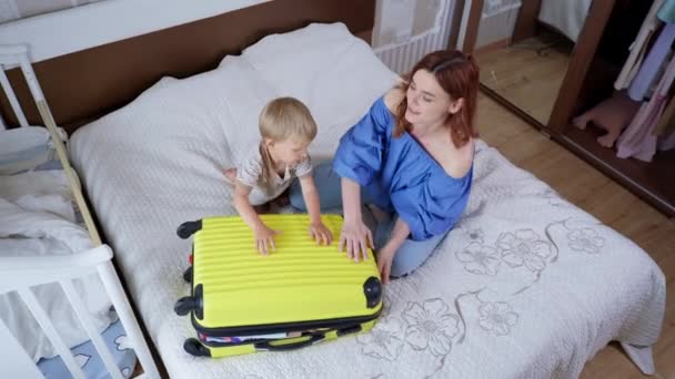 Vakantie voorbereiding, jong respectabele vrouwelijke ouder en haar eigen mannelijke kind veel plezier met het inpakken van een overvolle koffer voor familie reis — Stockvideo