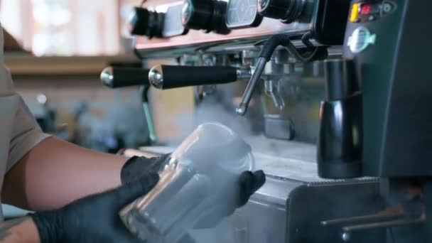 Giovane barista in guanti elabora bicchieri di vetro trasparente per cocktail con l'aiuto di vapore caldo utilizzando macchina da caffè professionale, piccola impresa — Video Stock