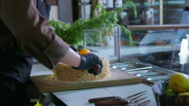 Pékségek, egy profi női szakács kesztyűben felvágott frissen sült desszert torta késsel vágódeszkán étteremben — Stock videók