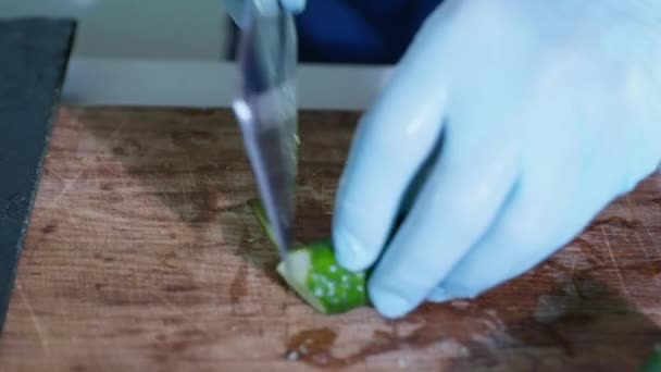 Cook with gloves slices of fresh healthy cucumbers for preparing healthy food or salad on cutting board with knife, proper nutrition — Stock Video