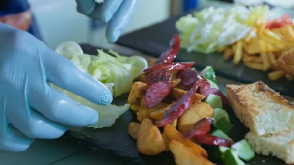 レストランフードプロのシェフがキッチンカフェでプレートにグリルした狩猟ソーセージとおいしい揚げポテトを準備します — ストック動画