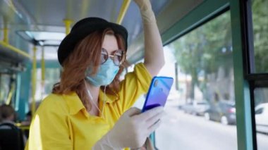 Gözlüklü genç bayan yolcu, karantina sonrası toplu taşıma araçları ile seyahat ederken tıbbi maske ve eldiven takıyor.