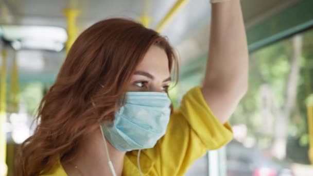 Vrouwelijke passagier met medisch masker en handschoenen ter bescherming tegen virus tegen infectie tijdens de coronavirus pandemie luistert naar muziek op de hoofdtelefoon tijdens het rijden stadsbus tijdens sociale afstand — Stockvideo