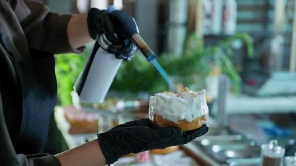 Słodycze, proces wytwarzania pączków przez szefa kuchni przez cukiernika, piekarz spala krem białkowy na pączku palnikiem gazowym w kuchni piekarni — Wideo stockowe